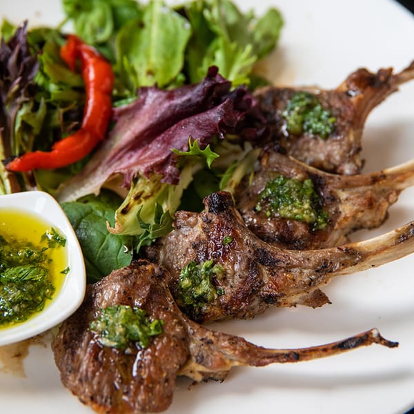 Grilled lamb chops with green herb sauce, a side salad, and a red chili pepper.