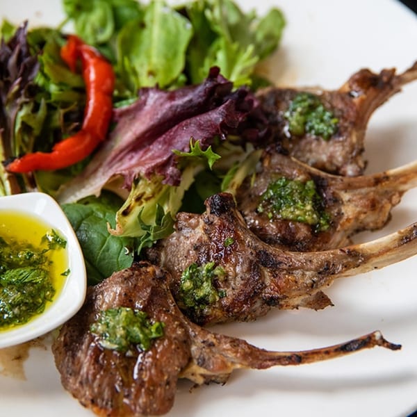 Grilled lamb chops with green herb sauce, a side salad, and a red chili pepper.