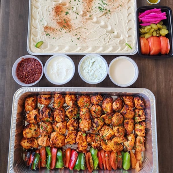 Lebanese catering spread with chicken shish tawook, hummus, pickled vegetables, and various sauces.
