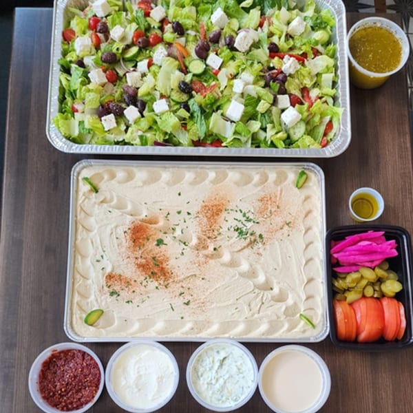 Large catering trays of fresh salad, hummus, pickled vegetables, and various dips from Mary'z Mediterranean Cuisine.