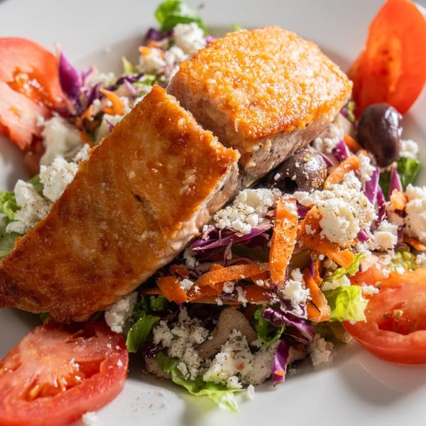 Crispy salmon fillet over a fresh salad with tomatoes, olives, and crumbled feta cheese.
