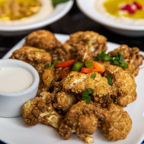Crispy fried cauliflower florets with a side of white dipping sauce, garnished with peppers and parsley.