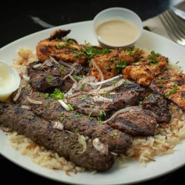 A Lebanese mixed grill platter with chicken, beef, and kafta kebabs over rice, with sauces.
