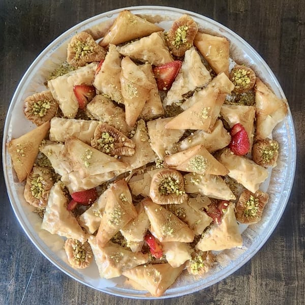 A large platter of assorted Lebanese baklava, garnished with pistachios and strawberries.